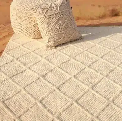 Textured woven rug in a diamond pattern with matching decorative cushions placed outdoors