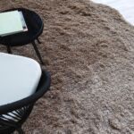 A brown Curvy Shaggy Area Rug with a plush texture and organic silhouette styled with a modern black side table.