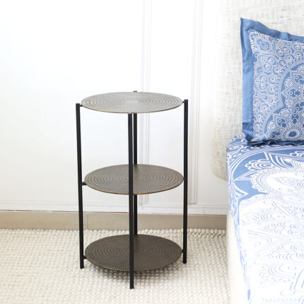 Round wooden side table with black metal base placed beside the bed – modern bedside furniture