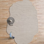 Off-white wool rug with wavy organic edges and carved wave texture on a wooden floor.