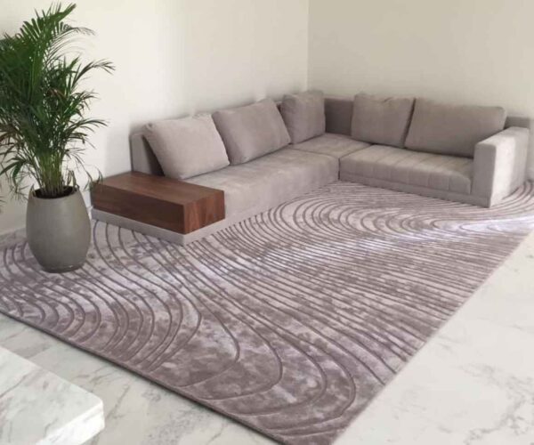 Large contemporary ripple texture rug in soft grey/taupe, featuring a sculpted wave pattern that flows into a modern L-shaped sectional sofa.