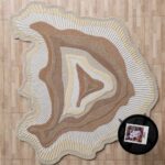 A Sculptural Earth Tone Rug with organic concentric layers in beige and cream, featuring hand-carved textured ridges on a wooden floor.