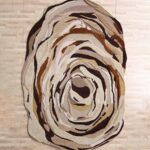 A large Shaped Multicolor Area Rug with a hand-carved vortex pattern in brown and cream tones.