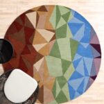A Modern Geometric Round Rug featuring a colorful mosaic of blue, green, and orange triangles on a light wooden floor.