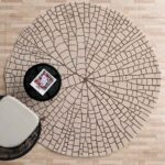 A handmade shaped rug in beige and brown with a radial carved mosaic pattern on a light wooden floor.