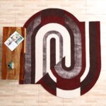 A Modern Geometric Shaped Rug in maroon, grey, and white with a unique interlocked horseshoe silhouette next to a wooden table.
