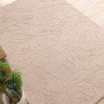 A premium luxury carpet featuring a handmade beige rectangle rug with a deep, hand-carved architectural texture.